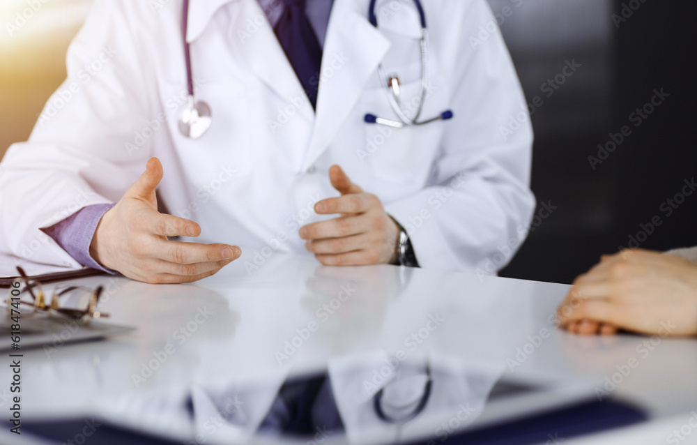 Unknown male doctor and patient woman discussing something while sittingin a darkened clinic, glare of light on the background. Close-up of hands Unknown male doctor and patient woman discussing something while sittingin a darkened clinic, glare of light on the background. Close-up of hands