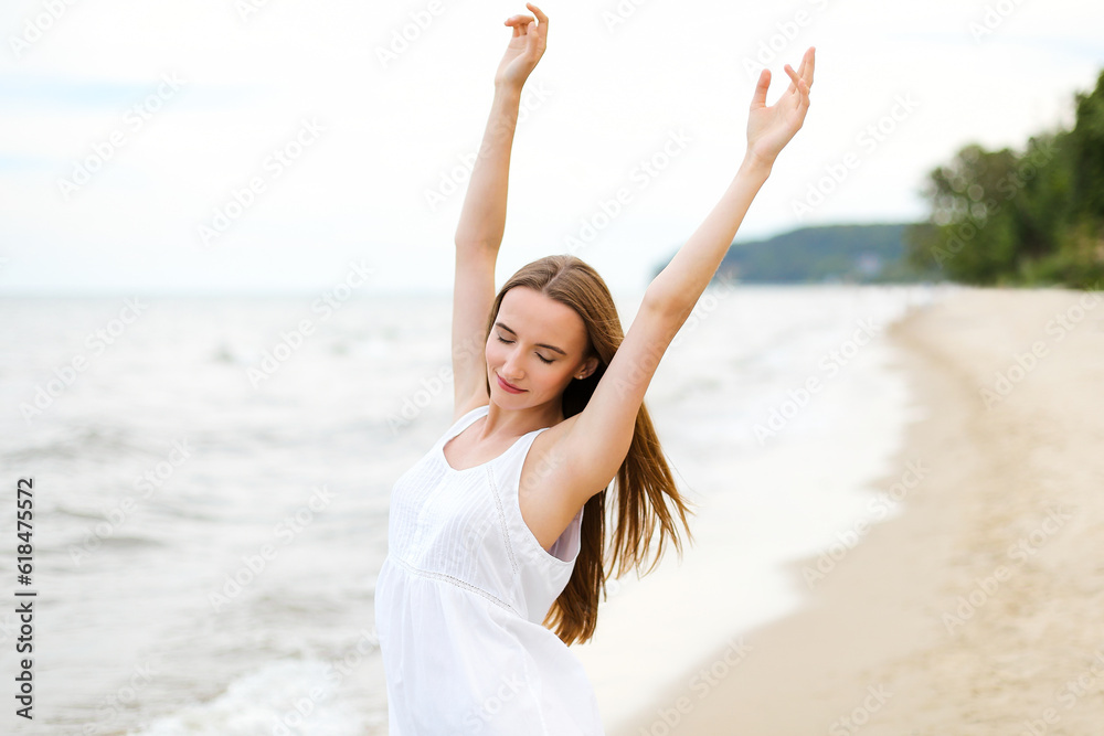 Happy smiling woman in free happiness bliss on ocean beach standing with raising hands. Portrait of a multicultural female model in white summer dress enjoying nature during travel holidays vacation Happy smiling woman in free happiness bliss on ocean beach standing with raising hands. Portrait of a multicultural female model in white summer dress enjoying nature during travel holidays vacation