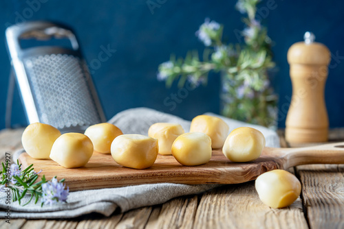 Smoked mozzarella balls on wooden cutting board, rosemary, napkin, grater, salt shaker over wooden table