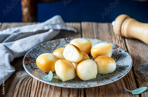 Smoked mozzarella balls in a grey plate with sage leaves, napkin over wooden table, chair backside