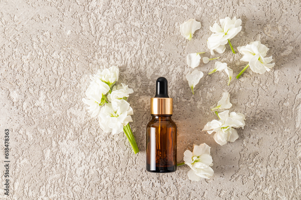 Cosmetic bottle with amber glass dropper with cosmetic product, serum or oil for face and body skin care. Top view. white flowers.