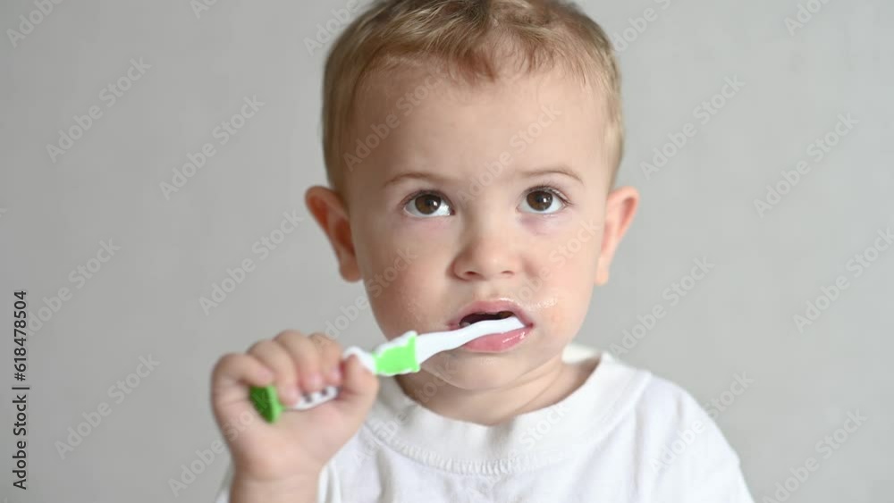 the kid is brushing his teeth with a toothbrush on a gray background. Oral hygiene. 