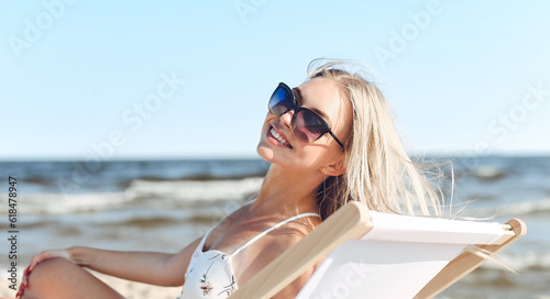 Happy blonde woman wearing sun glasses and relaxing on a wooden deck chair at the ocean beach