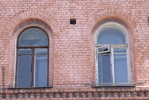 Front view of two antique rounded windows against the background of red brick walls, facade of an old house, grunge.