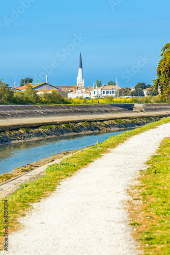 Black and white bell tower of Sainte-Etienne church in Ars-en-Ré, France seen from the path of the canal