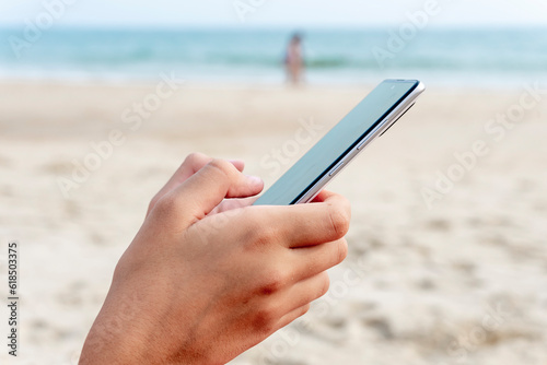 Closeup of hands holding and using smartphone on the beach on vacations. Travel insurance. Copy space.