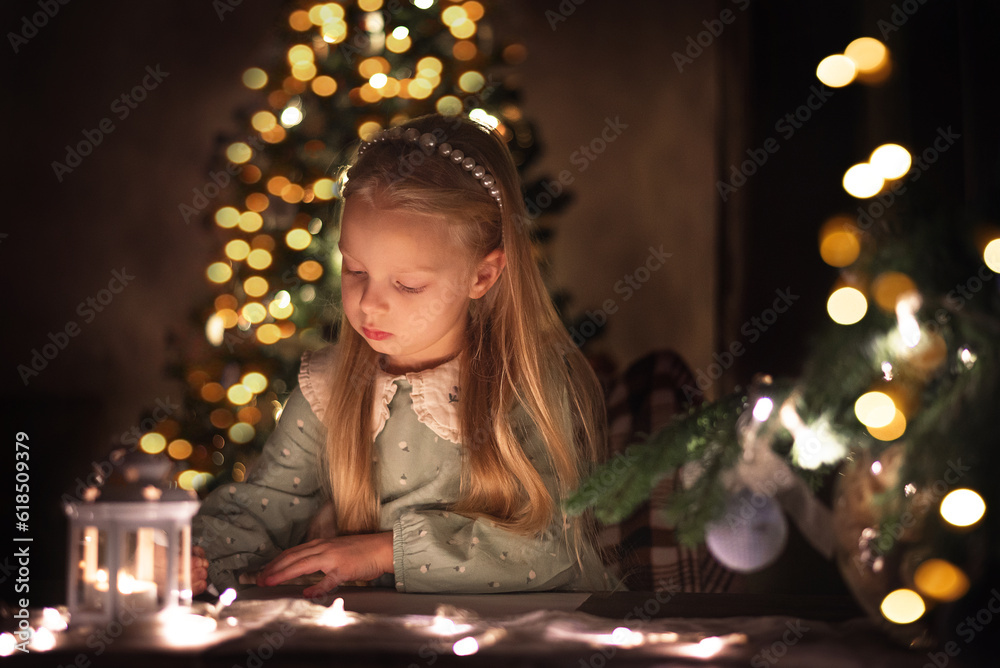 A little girl writes a letter to Santa Claus on the background of a Christmas tree