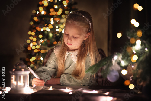 A little girl writes a letter to Santa Claus on the background of a Christmas tree