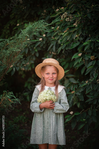A little beautiful blonde girl in a green dress and a straw hat with a bouquet of hydrangeas