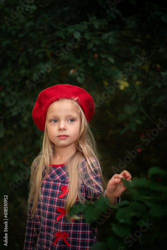 Portrait of a blonde little girl in a red beret and a plaid dress