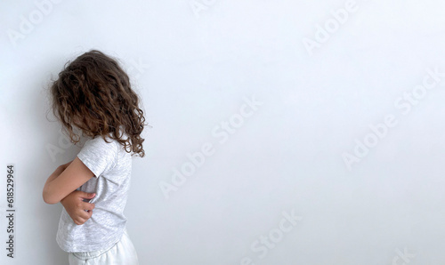 A girl with curly hair, turned away, stands with her head down on a white background.