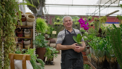 Happy senior Florist holding flower standing inside horticulture store. older male person wearing apron in local business Flower Shop © Marco