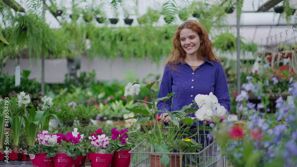 Happy female customer shopping at Flower Shop pushing cart selecting plants and flowers