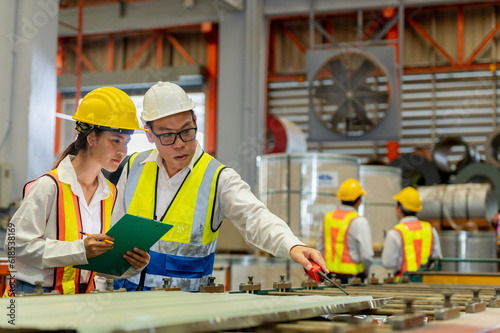 partner woman engineer assistant in helmet inspection check heavy machine construction installation in industrial metal roof roll sheet factory with colleague manager. partnership operation factory