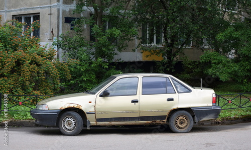 An old rusty light car is parked near a residential building, Iskrovsky Prospekt, Saint Petersburg, Russia, June 30, 2023