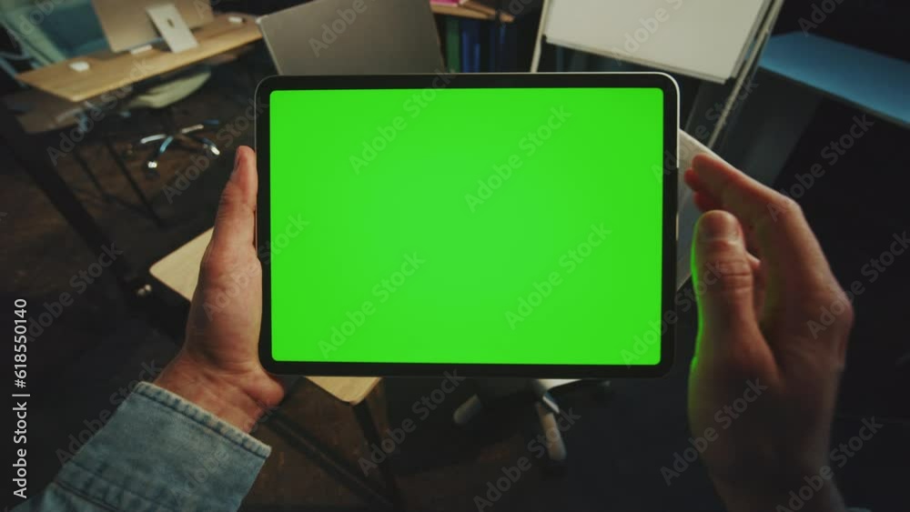Close up hands man holding scrolling a tablet computer with a horizontal green screen in office. Mock-up display. Device. Apartment