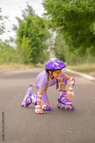 Girl in purple T-shirt, helmet and full sports protective gear gets up from knee with positive attitude after fall.h. Protective set against injuries and bruises. Life and health insurance photo