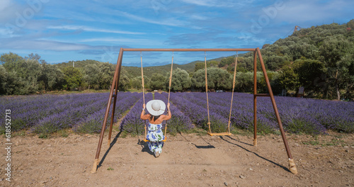 young woman with white straw hat plays with the swing in front of a lavender field
