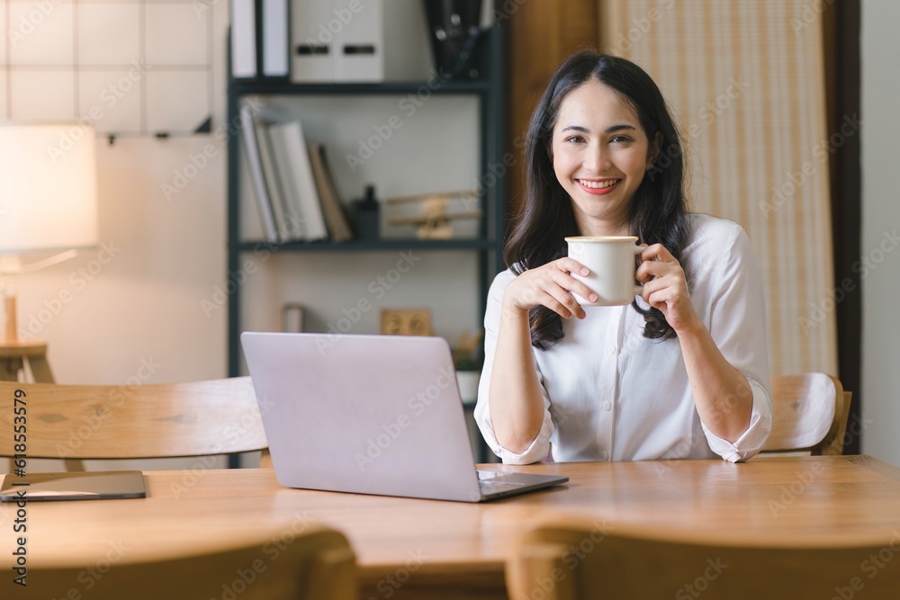 A millennial Asian businesswoman is sitting and working with laptop computer in her home kitchen, while also enjoying a relaxing cup of coffee. A millennial Asian businesswoman is sitting and working with laptop computer in her home kitchen, while also enjoying a relaxing cup of coffee.