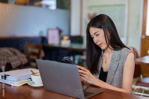 Portrait, Asian woman sitting on video call with colleague, consult about work that was sitting in bakery cafe, talk friends listen audio through headset cable that plugs into phone.