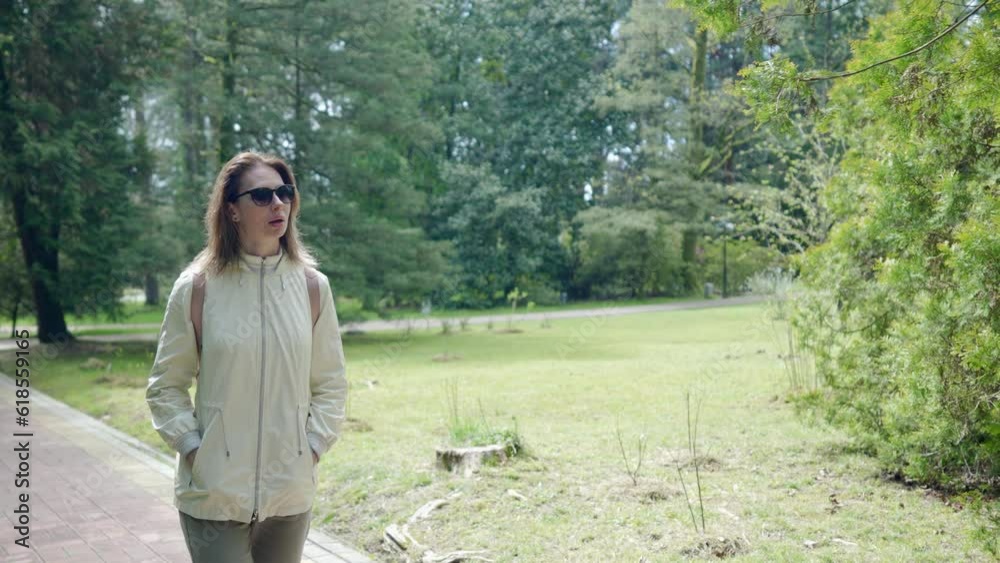 single middle aged woman walking alone in park in sunny day, admiring beauty of nature single middle aged woman walking alone in park in sunny day, admiring beauty of nature