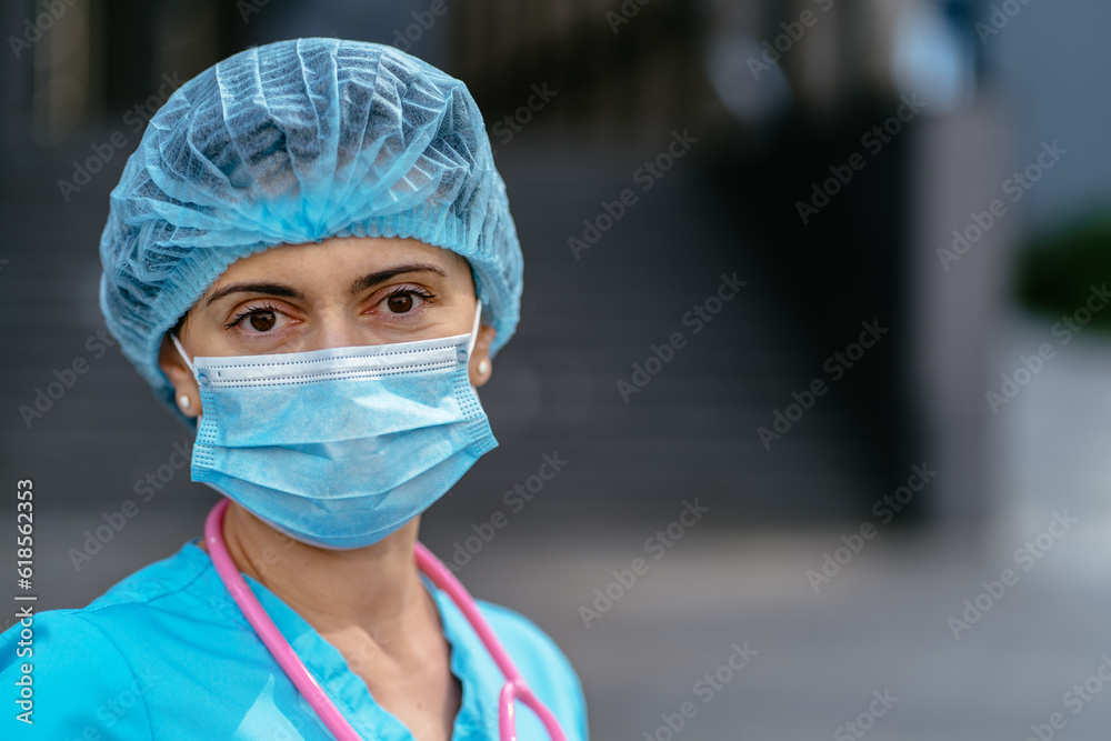 Medicine, profession and healthcare concept. Close up of face female doctor or nurse wearing a protective face mask and uniform with stethoscope next to hospital on background, outdoor shot. Medicine, profession and healthcare concept. Close up of face female doctor or nurse wearing a protective face mask and uniform with stethoscope next to hospital on background, outdoor shot.