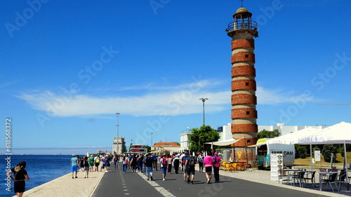 Viele Touristen wandern entlang des Flusses Tejo zum Turm von Belem vorbei an einem alten Leuchtturm