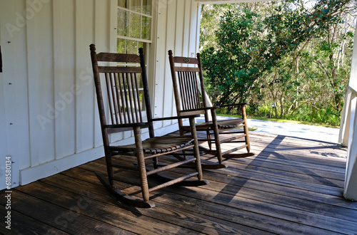 Old vintage rocking chairs sitting on a colonial style Florida house porch with trees in background