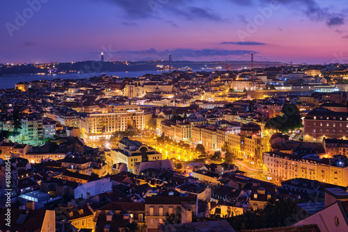 Fototapeta Naklejka Na Ścianę i Meble -  Night view of Lisbon famous view from Miradouro da Senhora do Monte tourist viewpoint of Alfama and Mauraria old city districts, 25th of April Bridge in the evening twilight. Lisbon, Portugal