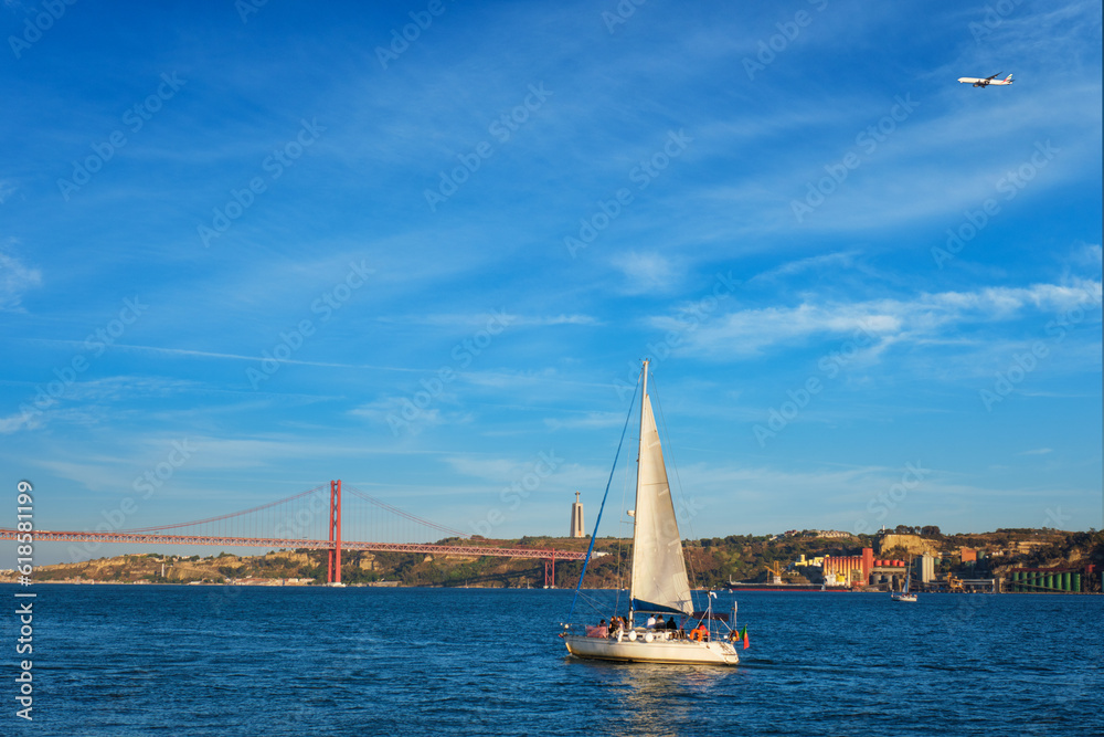 View of 25 de Abril Bridge famous tourist landmark over Tagus river, Christ the King monument and a tourist yacht boat at sunset. Lisbon, Portugal