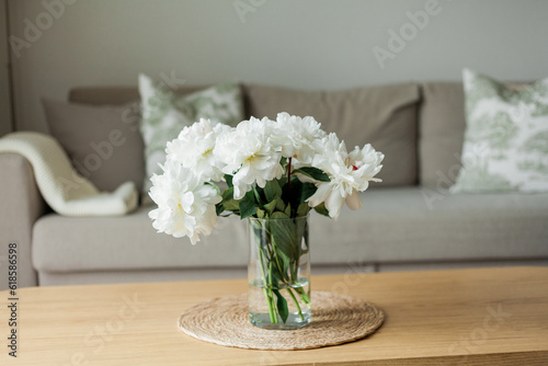 Home cozy interior. Bouquet of peonies in a glass vase on a wooden coffee table. Spring.