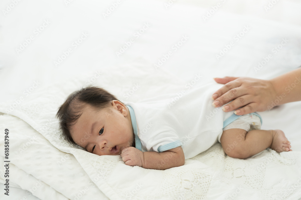 Newborn baby sleeping in prone position on bed. Newborn baby or infant lying on white bed while mother’s hands takes care carefully. Family, love and new life concept Newborn baby sleeping in prone position on bed. Newborn baby or infant lying on white bed while mother’s hands takes care carefully. Family, love and new life concept