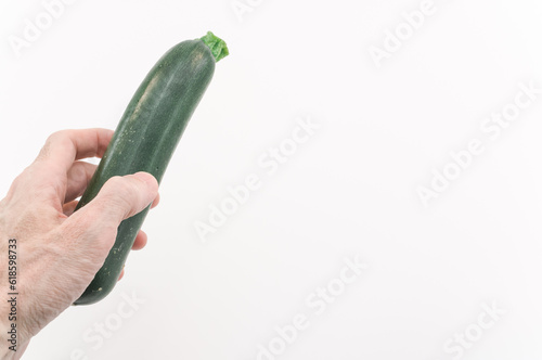 immagine primo piano di mano che regge ortaggio fresco zucchino da agricoltura biologica su superficie bianca photo