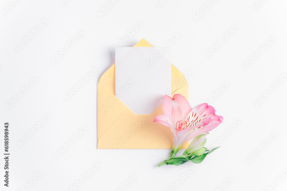 Yellow envelope with blank card and pink alstroemeria flower on white background. Birthday, Valentines day, Mothers day, Womens day concept. Top view, flat lay, mock up