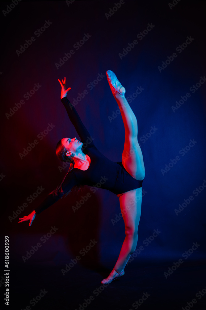 Obraz premium A girl gymnast in a swimsuit does tricks on a white and dark background. Front view
