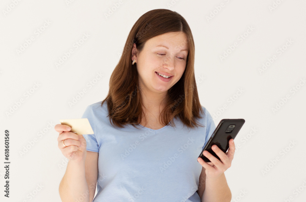 Online shopping. Portrait of smiling pregnant woman paying with plastic credit card on smartphone app, standing with mobile phone and bank card against white background Online shopping. Portrait of smiling pregnant woman paying with plastic credit card on smartphone app, standing with mobile phone and bank card against white background