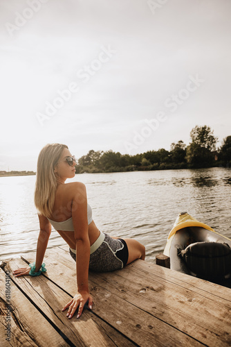 girl sits on a dock and looks at the river a kayak is tied to the dock