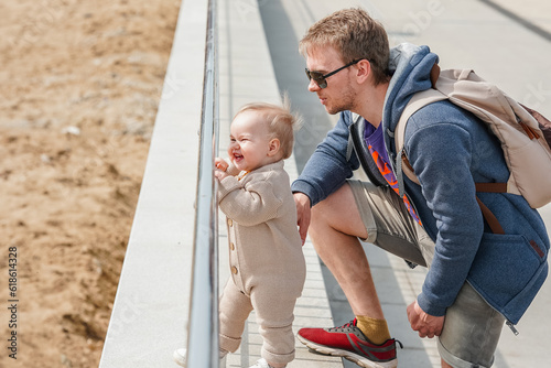 Charming little baby toddler next to her father on the embankment looking at the sea © KseniaJoyg
