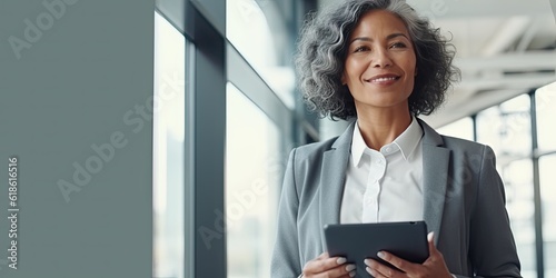 Smiling happy middle-aged BIPOC businesswoman executive CEO in a business suit using a computer to work with a client in an office setting -room for copy text, generative AI 