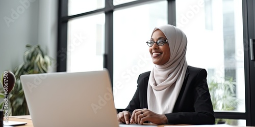 Smiling happy  BIPOC businessman executive CEO in a business suit and Hijab using a computer to work with a client in an office setting -room for copy text, generative AI 

