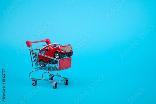 Tableau sur toile A red toy car in a toy supermarket cart on a blue background.