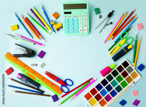 School supplies lie in a circle on the table on a blue background, pens, paints, pencils, scissors, a calculator. Concept back to school. Copy space for text, flat lay, top view. Background picture