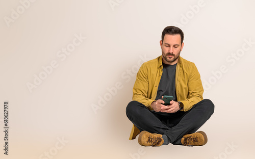 Serious young handsome businessman reading text messages on smart phone while sitting with legs crossed. Male professional dressed in casuals checking social media on cellphone against background © Moon Safari