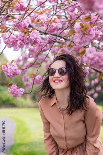 Woman in her mid 30 in park with blooming cherry tree or sakura, springtime in UK. Enjoying life and sunny day with warm weather