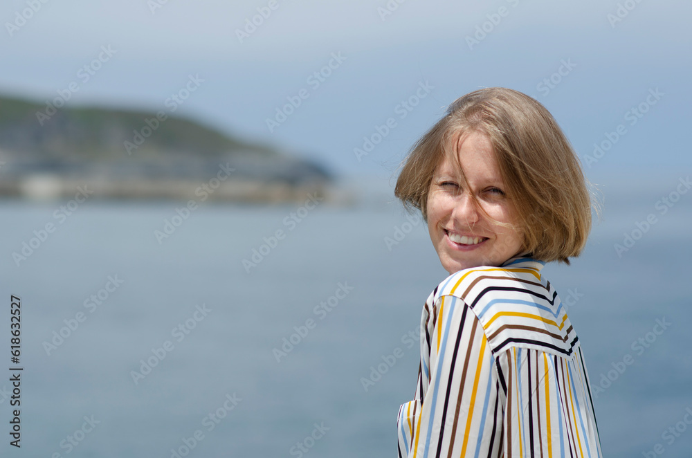 Young woman smiling confidently at the camera on a sunny day at the seaside with a soft focus background Young woman smiling confidently at the camera on a sunny day at the seaside with a soft focus background