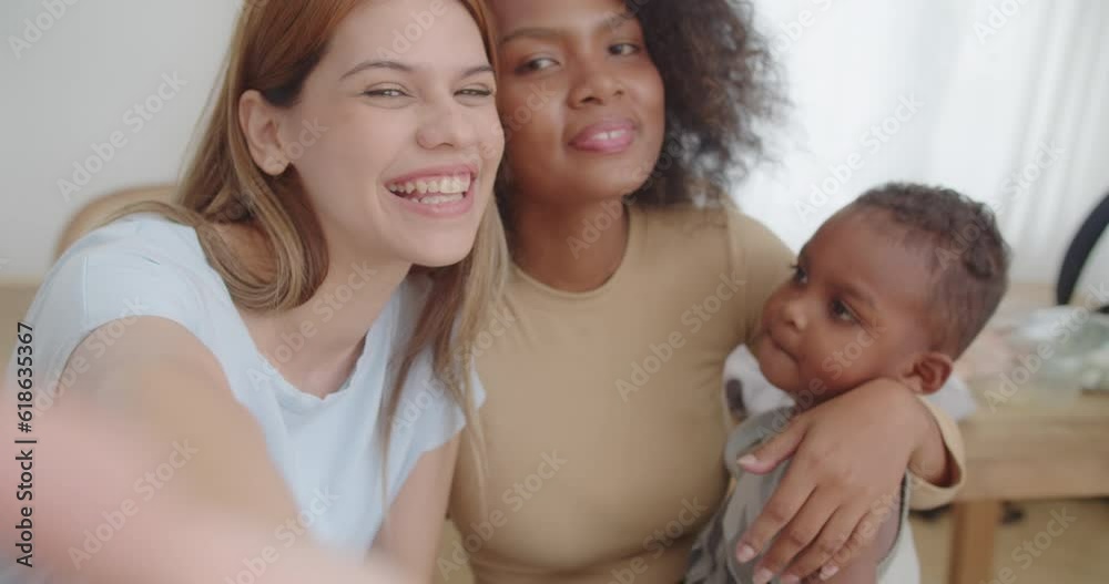 Happy young homosexual female gay lesbian couple with son toddler baby boy is making taking selfie together or video call to friends or relatives in a living room at home, Concept of LGBTQ+ Happy young homosexual female gay lesbian couple with son toddler baby boy is making taking selfie together or video call to friends or relatives in a living room at home, Concept of LGBTQ+