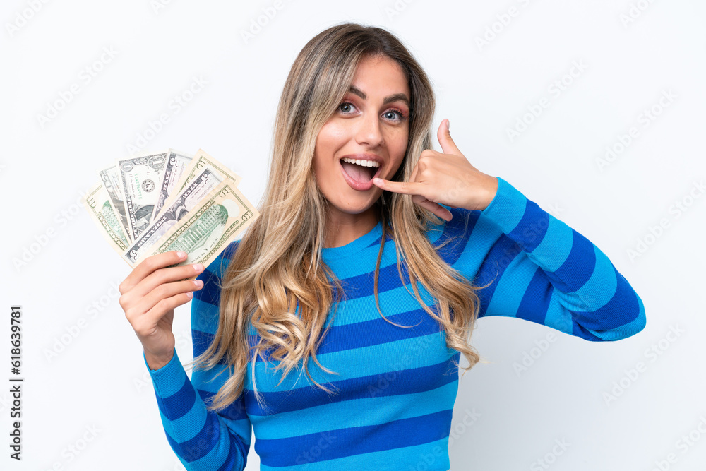 Young Uruguayan woman taking a lot of money isolated on white background making phone gesture. Call me back sign Young Uruguayan woman taking a lot of money isolated on white background making phone gesture. Call me back sign