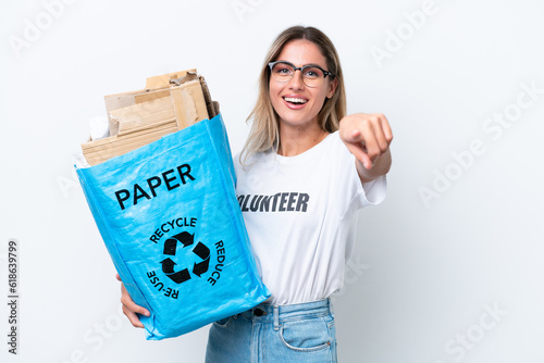 Young pretty Uruguayan woman holding a recycling bag full of paper to recycle isolated on white chroma background points finger at you with a confident expression