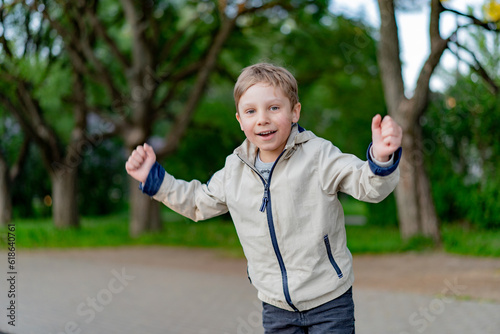 happy little caucasian boy triumphant with raised hands in park