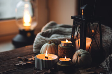 Cozy autumn composition with aromatic candle, pumpkins, wool sweater, leaves, cinnamon. Aromatherapy on a grey fall morning, home atmosphere of cosiness and relax. Wooden background close up.